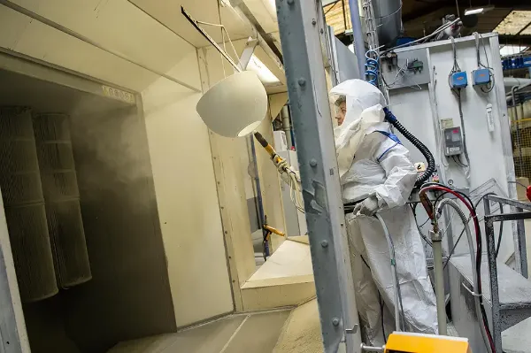 Travailleuse équipée de protection individuelle appliquant de la peinture poudre