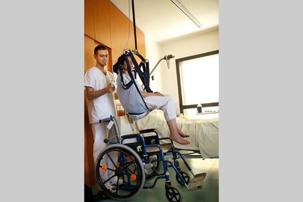 Déplacement d’un patient de son lit au fauteuil par un infirmier à l’aide d’un lève personne sur rails