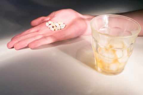 Photo de médicaments dans la main d’une personne, un verre d’alcool au premier plan 