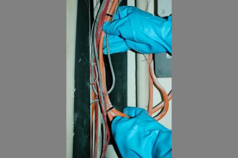 Dénudage par un électricien d’un ancien cable électrique dans lequel se trouve une tresse d’amiante pour sa résistance au feu