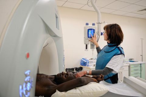 intervention avant lancement du scanner d’une opératrice équipée d'un tablier de plomb avec protège-thyroïde  dans un hôpital