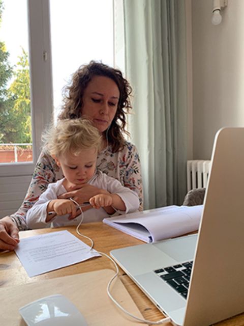 Photo représentant une salariée en télétravail à son domicile, assise devant son ordinateur avec son enfant sur les genoux