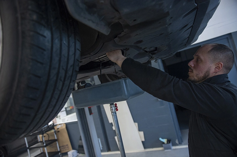 Un salarié travaille sous une voiture, les bras en l'air.