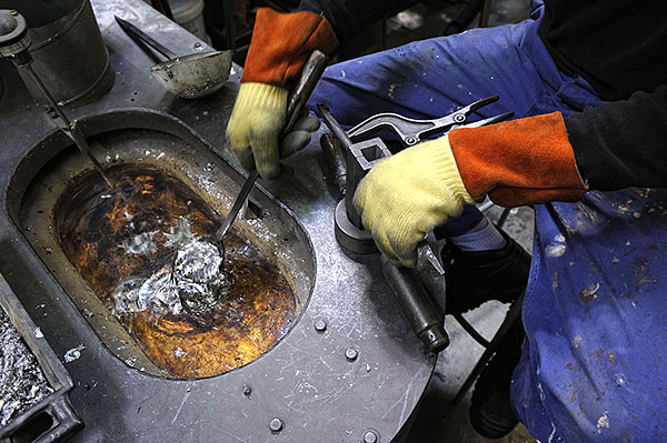 coulée de plomb en fusion dans une fabrique de plombs de pêche, avec un creuset équipé d'un anneau aspirant permettant un captage à la source